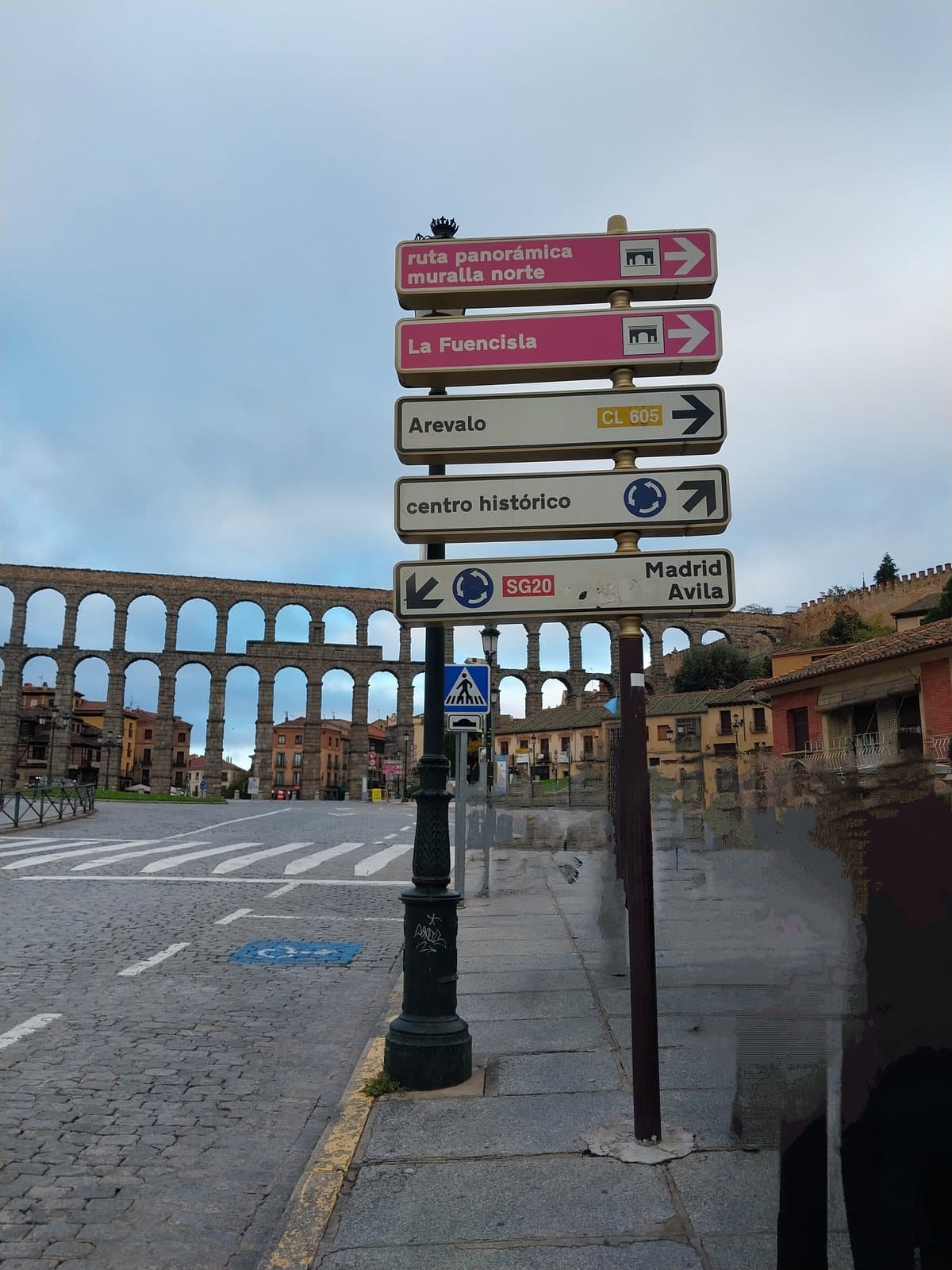 Placas de trânsito em espanhol com o aqueduto de Segóvia ao fundo
